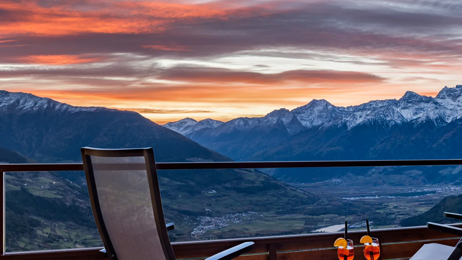 Terrace with two loungers and two aperitif glasses, the Vinschgau valley and the Ortler group glowing at dusk behind